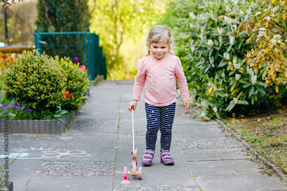 little toddler girl walking in park on sunny spring day. Cute adorable child playing with pushing wooden toy animal on wheels