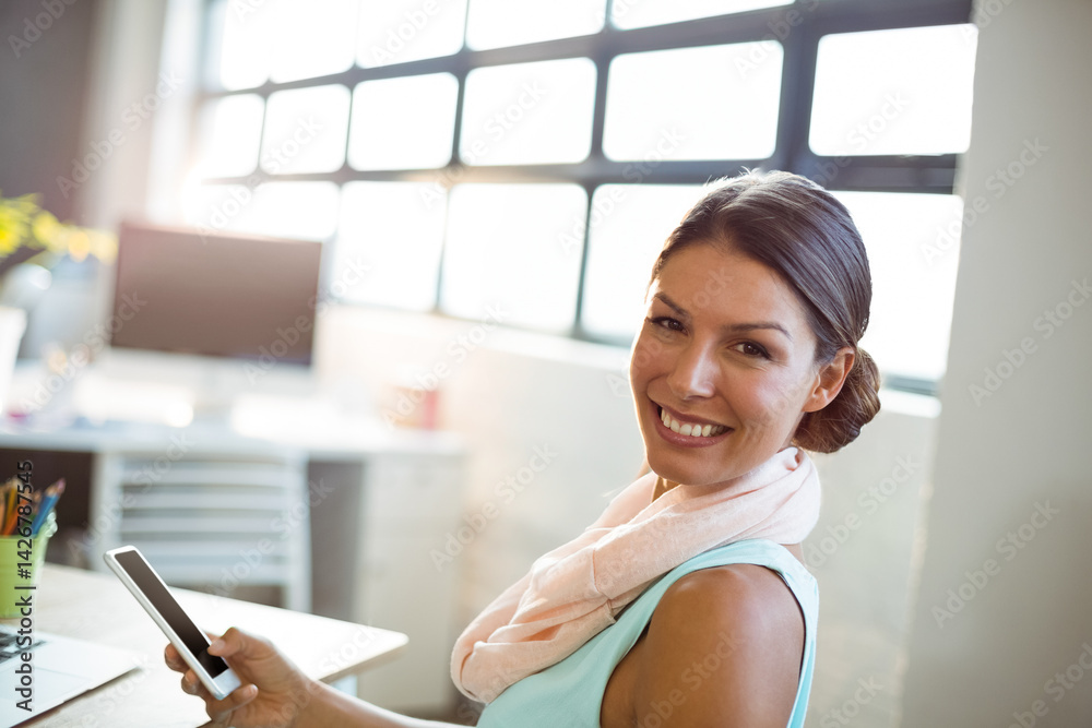 Woman sitting at desk in bright modern office, holding smartphone with laptop and plant, copy space