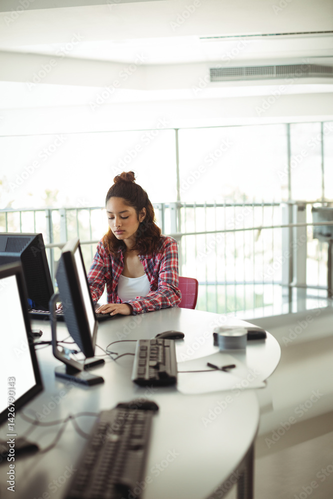bi-racial teenage girl typing at computer lab desk, with dual monitors and tape dispenser