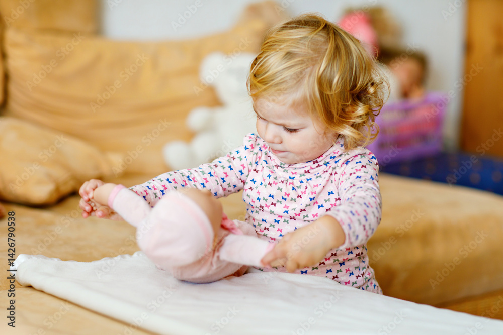 Adorable cute little toddler girl playing with doll. Happy healthy baby child having fun with role game, playing mother at home or nursery. Active daughter with toy.