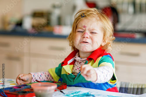 Obraz na płótnie Sad crying baby girl learning painting with water colors. Frustrated Little toddler child drawing at home, using colorful brushes. Angry child in hysteric crisis. w salonie