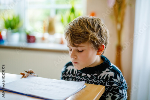Obraz na płótnie Hard-working happy school kid boy making homework during quarantine time from corona pandemic disease. Healthy child writing with pen, staying at home. Homeschooling concept w salonie