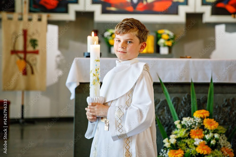 Little kid boy receiving his first holy communion. Happy child holding Christening candle. Tradition in catholic curch. Kid in a white traditional gown in a church near altar.