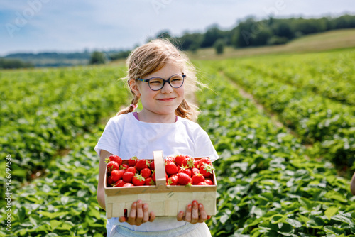 Obraz na płótnie Little girl picking strawberries on a strawberry farm. Happy child with eyeglasses and ripe berries on pick a berry field. Family summer time activity w salonie