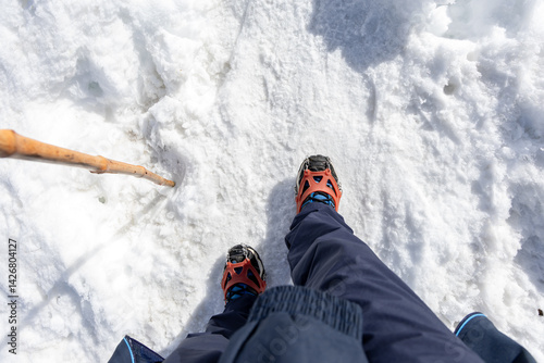man waking on snow with shoe crampons and stick at day