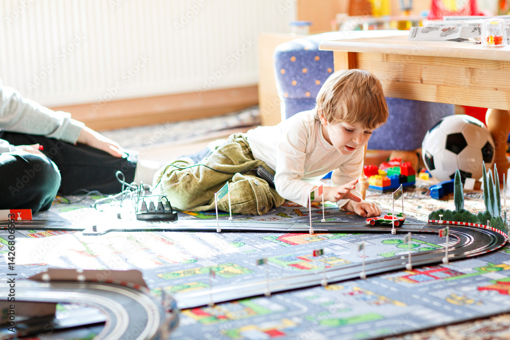 Father and son playing with racing cars on racetrack, indoors, with cars. Happy little preschool boy and young man having fun with indoor race game