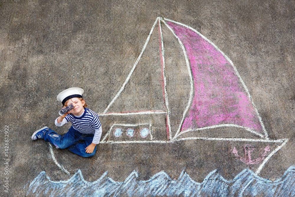 Little kid boy as pirate on ship or sailingboat picture painting with colorful chalks on asphalt. Creative leisure for children outdoors in summer. Child with captain hat and binoculars.