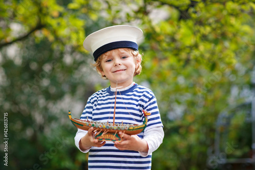 Obraz na płótnie Happy little kid boy in sailor capitain hat and uniform playing with sailor boat ship. Smiling preschool child dreaming and having fun. Education, profession, dream concept w salonie