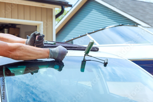 Skilled technician worker is replacing damaged windshield on vehicle, ensuring precise replacement windshield