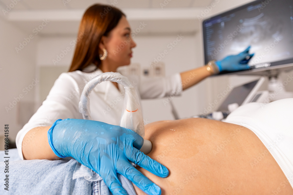 Close up pregnant woman lying in hospital ward and has uterus ultrasonographic diagnosis - female doctor scans her uterus and shows on screen with hand in medical gloves. Maternity, pregnancy concept.