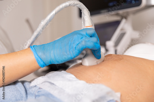 Obraz na płótnie Close up ultrasound scanner device in the hand of a professional doctor examining pregnant woman patient, doing abdominal ultrasound scanning. sonogram, sonography, sonographer, early pregnancy w salonie