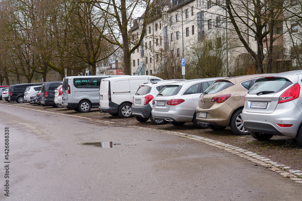 Cars parked along a street in an urban area on a cloudy day with trees lining the road Cars parked along a street in an urban area on a cloudy day with trees lining the road