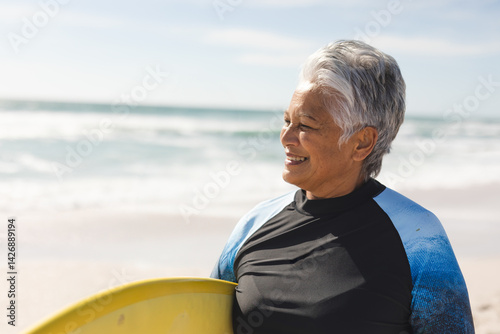 Photography Senior woman standing with yellow surfboard on beach in black or blue wetsuit, e