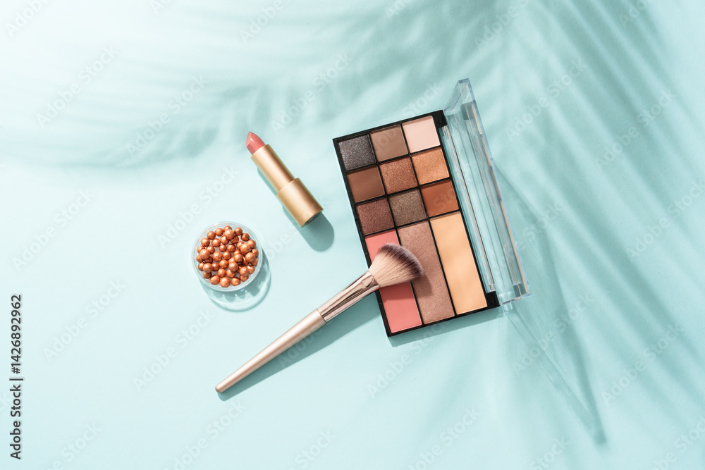 Make up products on blue background with palm shadows. Cosmetic palette, brushes and lipstick.