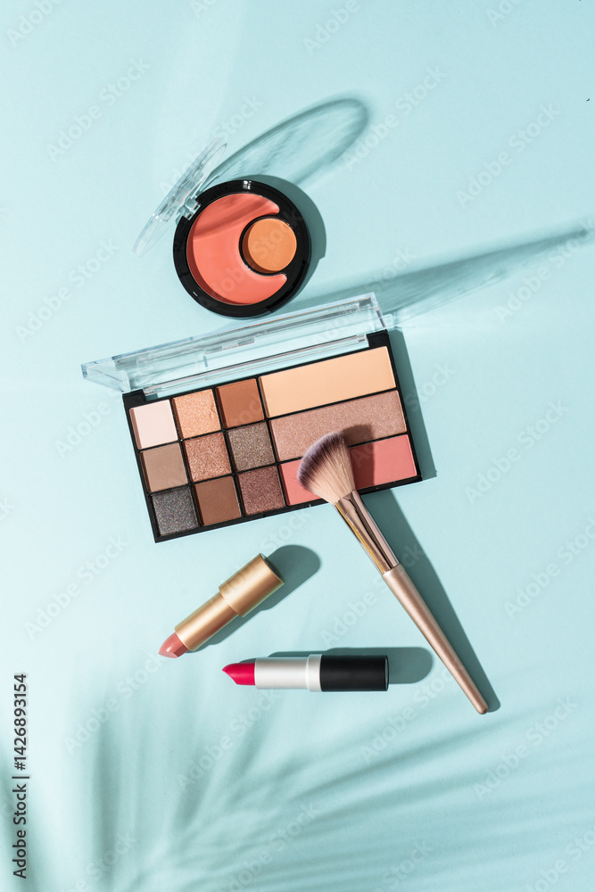 Make up products on blue background with shadows. Cosmetic palette, brushes and lipstick. Top view image.
