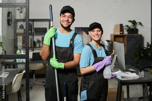 Portrait of colleagues in uniform smiling at camera while doing cleaning in team in office