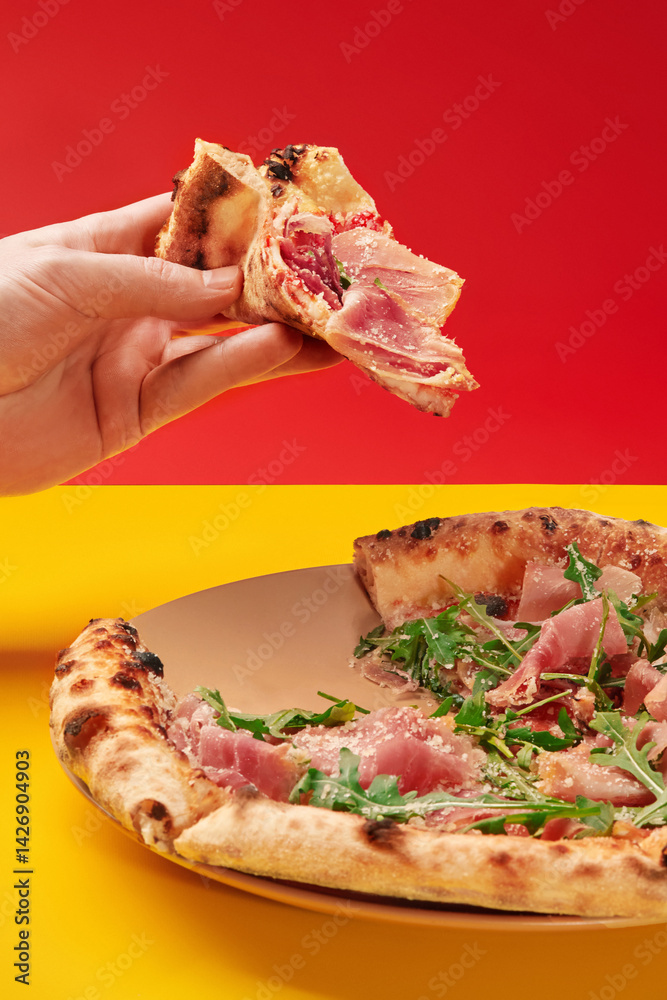 Hand holding slice of prosciutto pizza over pizza on plate