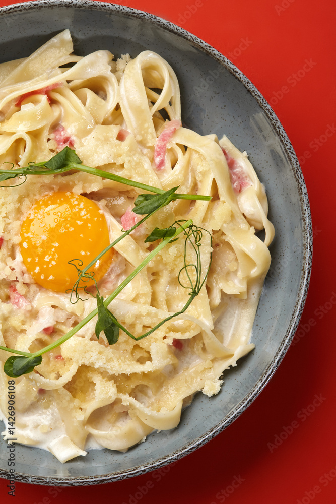 Creamy pasta carbonara with egg yolk and parmesan on red background