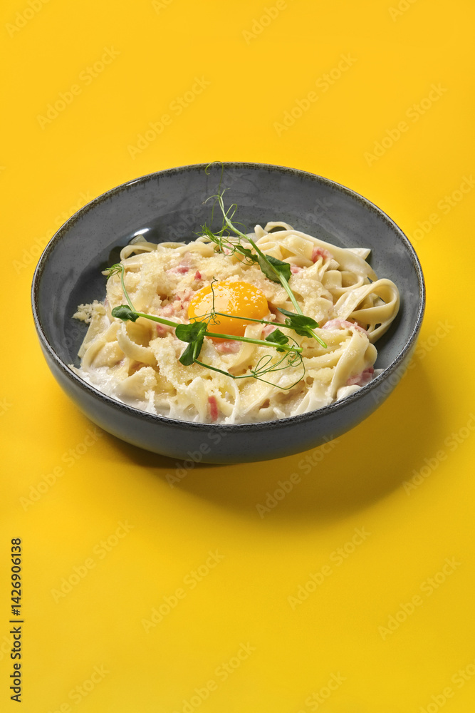 Creamy carbonara pasta with egg yolk and pea shoots on vibrant yellow background