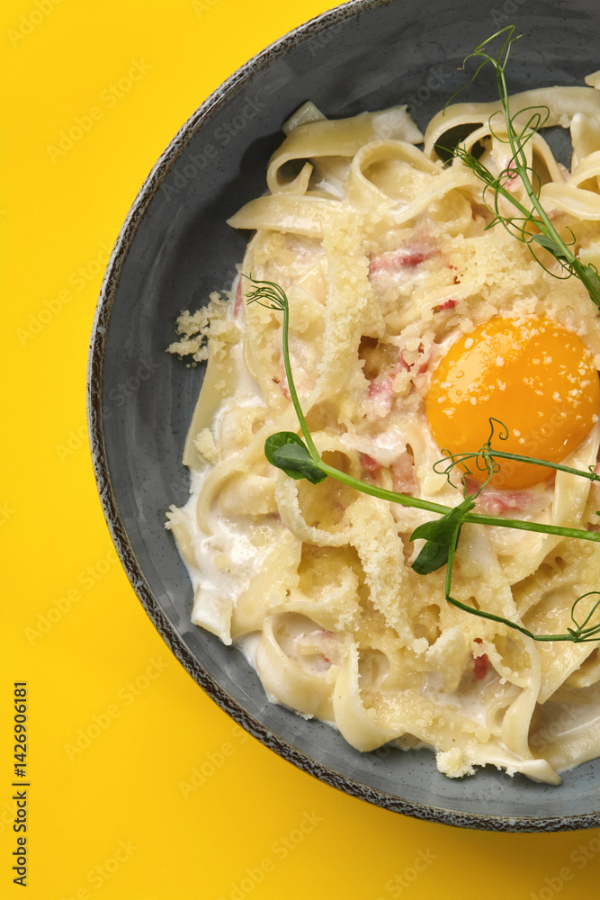 Delicious pasta carbonara with egg yolk and parmesan cheese on vibrant yellow background