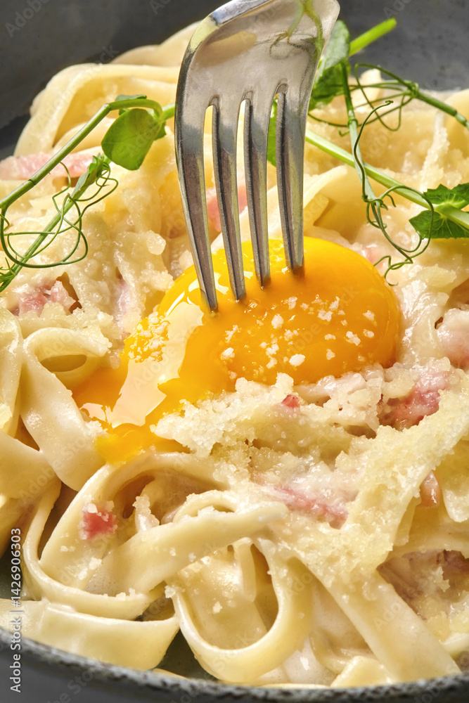 Fork piercing egg yolk in creamy carbonara pasta
