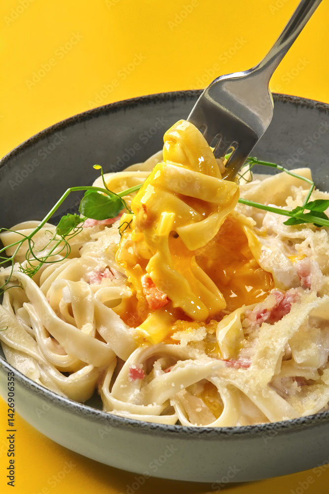 Fork lifting creamy carbonara pasta with egg yolk and parmesan cheese