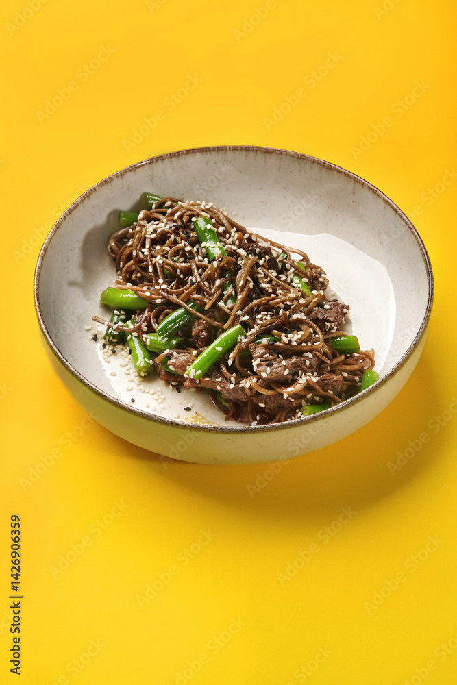 Soba noodles with beef and green onions on vibrant yellow background