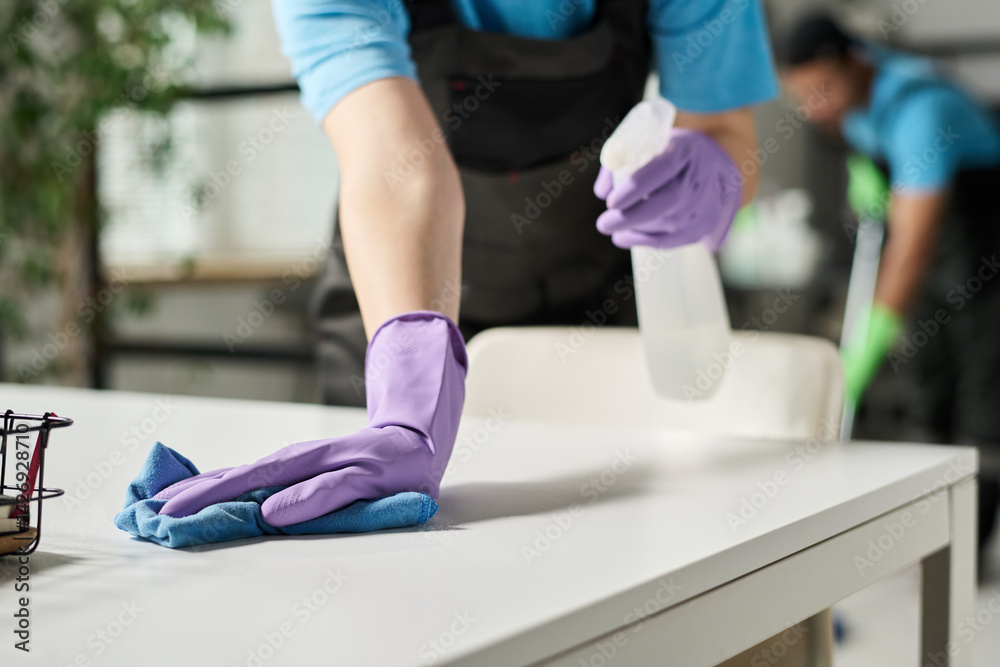 Close-up of worker in rubber gloves doing wet cleaning and wiping dust from furniture in office