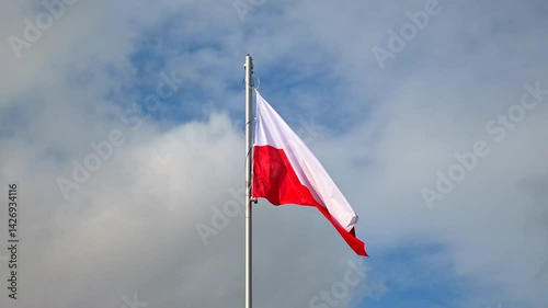 Polish flag flutters in the wind against a vivid blue sky, red and white stripes bright and clear, evoking national pride and freedom.
