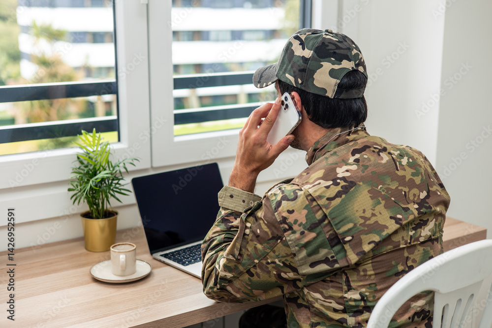 Obraz premium Soldier wearing camouflage uniform talking on smartphone and working from home