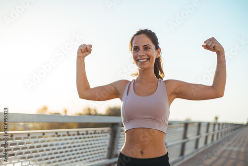 Obraz na płótnie Smiling Fit Woman Flexing Arms in Athletic Wear During Outdoor Workout w salonie