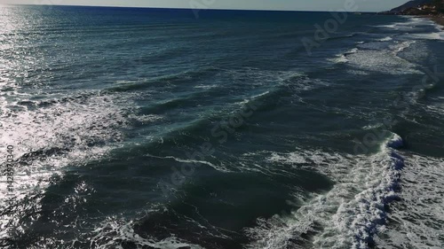 Gentle waves cascading over sandy beach, sunlight sparkling on rippling water surface, creating peaceful coastal scenery
