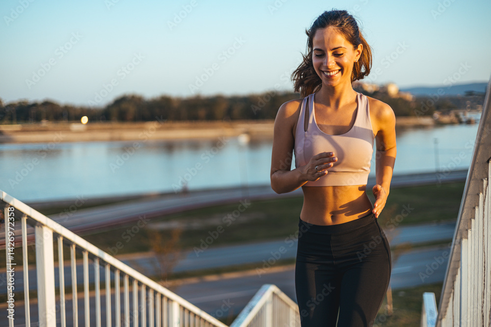 Smiling Young Woman Running Outdoors Along Riverbank at Sunset