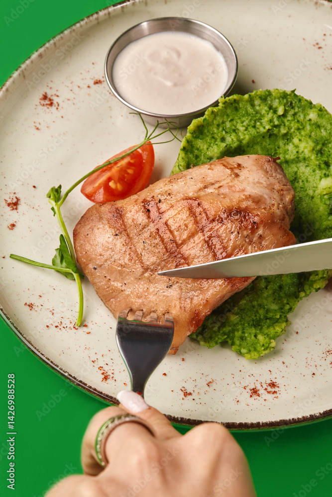 Woman eating grilled chicken breast with green puree and white sauce