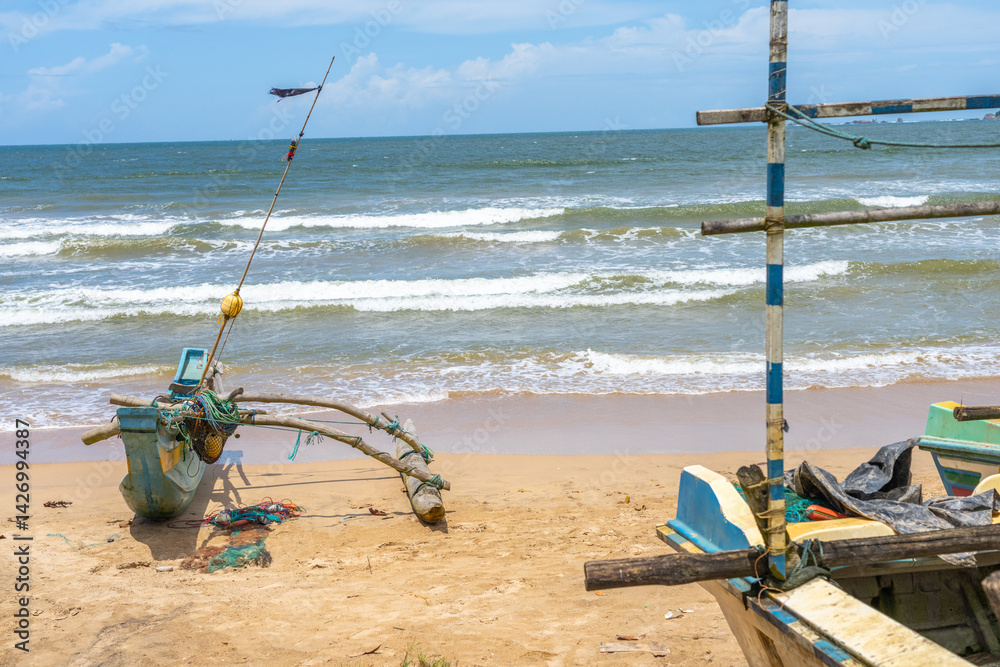 Colourful traditional style outrigger canoe with fishing nets and gear pulled up on beach.