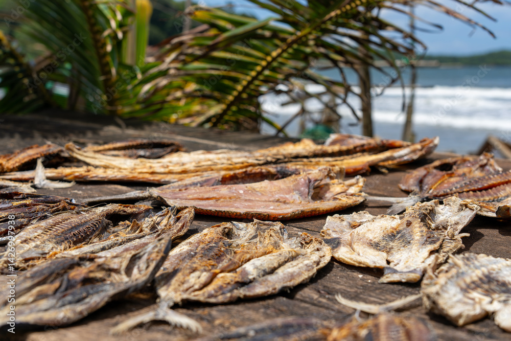 Dried fish laid out on old table in fish market stall line beach side of street under palm frond roof