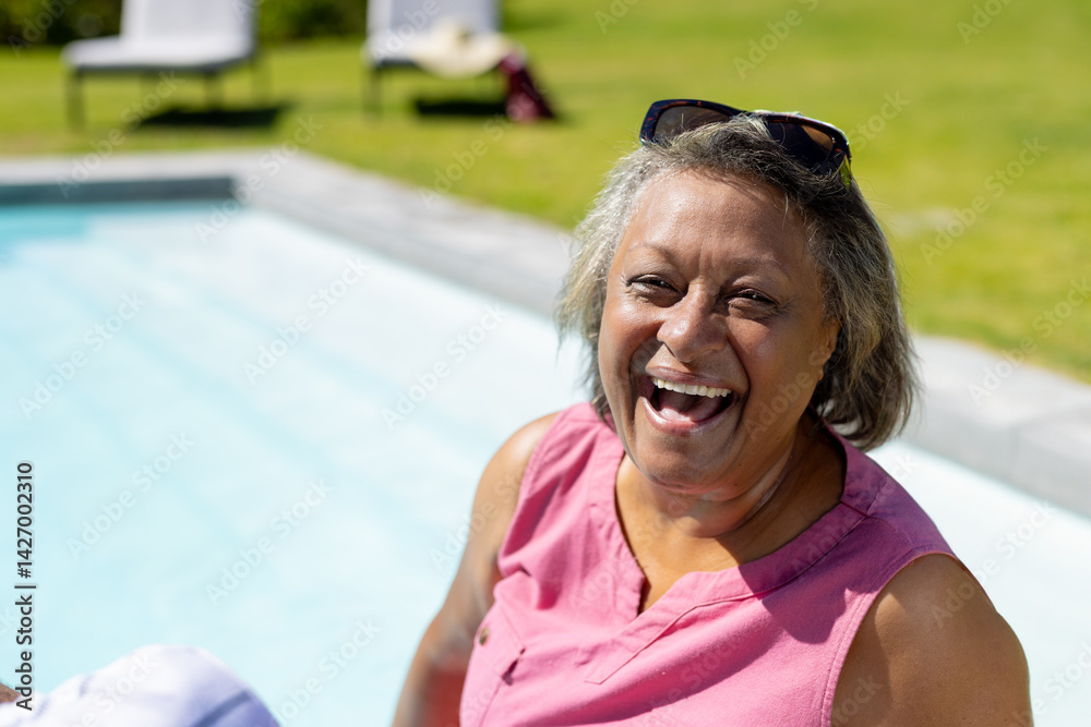 Relaxed senior woman enjoying sun on pool edge in backyard with sunglasses, copy space