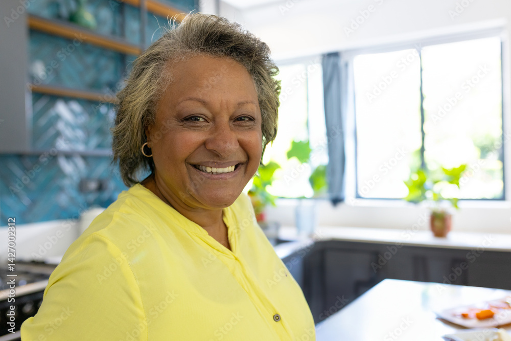 Senior woman standing in bright modern kitchen, with teal tile backsplash and potted plants