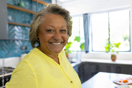 Obraz na płótnie Senior woman standing in bright modern kitchen, with teal tile backsplash and potted plants w salonie