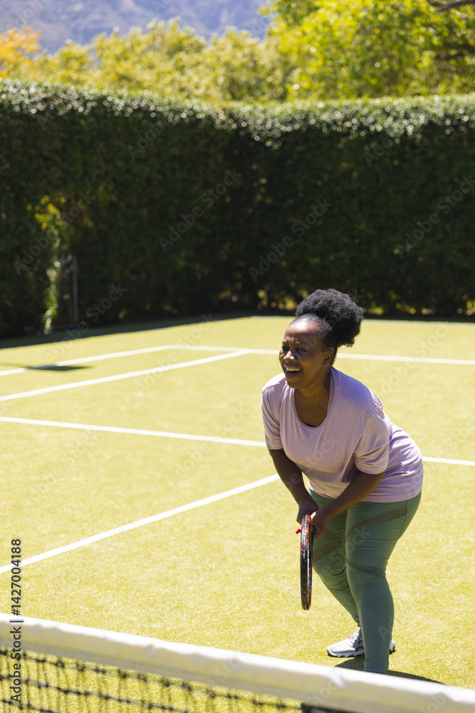 Mature African American woman holding tennis racket on tennis court behind net, copy space