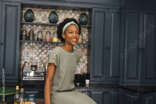 Obraz na płótnie African American woman sitting on kitchen island, surrounded by oil bottles and mosaic backsplash w salonie