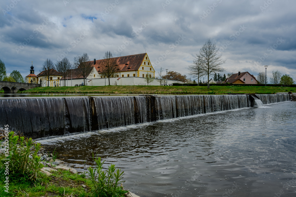 Fototapeta premium Picturesque waterfall and historic building beside tranquil waters under a cloudy sky