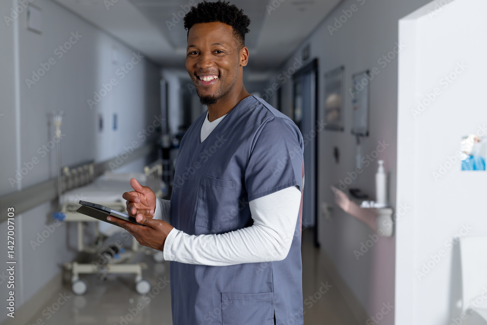 Young adult African American man standing in hospital corridor holding tablet near gurney