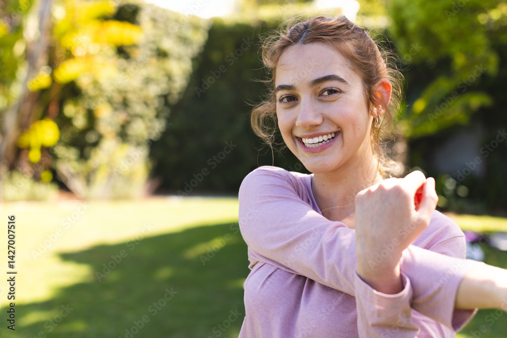 Woman stretching arm across chest in suburban backyard garden, enjoying sunny stretch, copy space