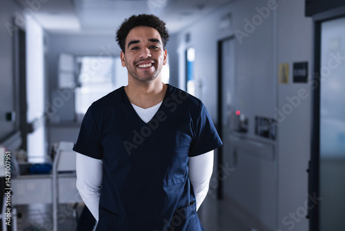 Obraz na płótnie Young adult male healthcare worker standing in hospital corridor, smiling with medical cart behind w salonie