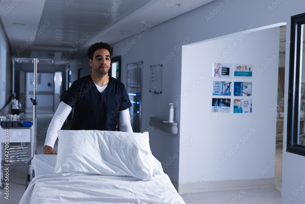 Young man pushing empty hospital bed down bright hospital corridor, with IV pole and supply trolley