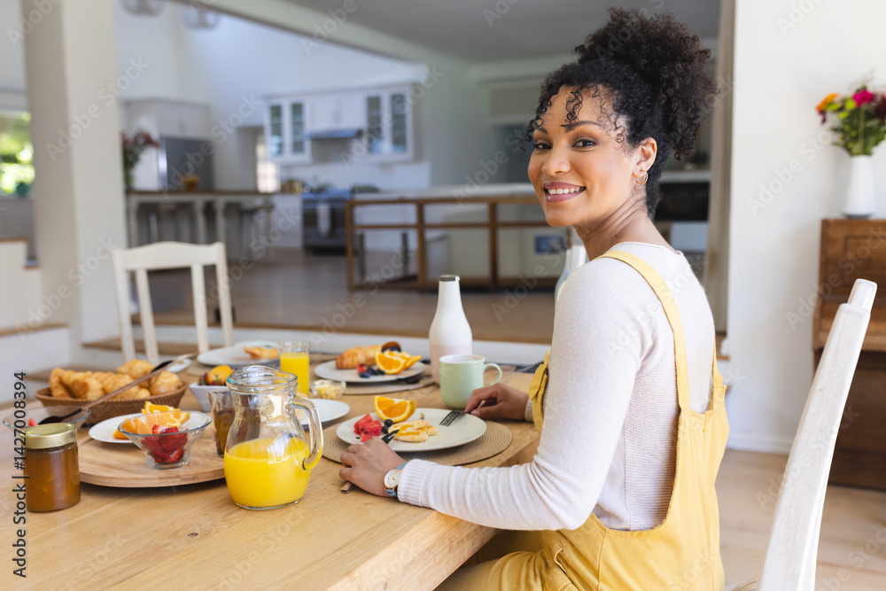 Woman sitting at dining table in open kitchen smiling over shoulder with juice pitcher, copy space