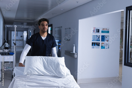 Obraz na płótnie Young man pushing empty hospital bed down bright hospital corridor, with IV pole and supply trolley w salonie