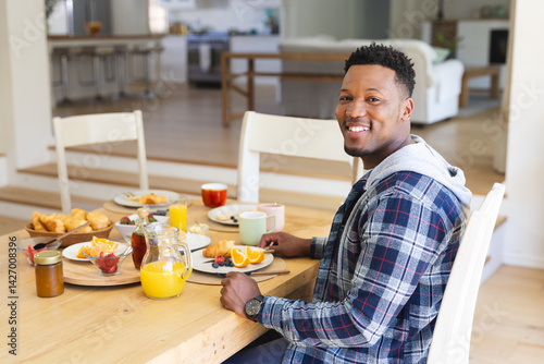 Obraz na płótnie African American man eating breakfast croissants at dining table in open plan home, copy space w salonie