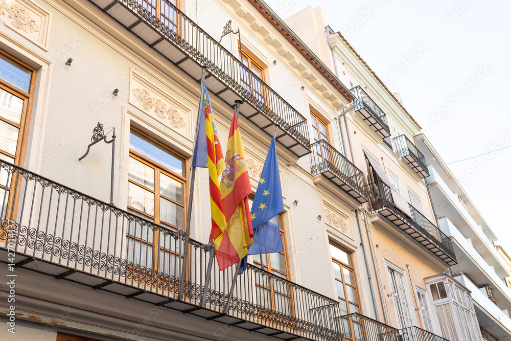 Two Spanish flags in the wind. Spanish flags and EU flag on the wall of a house. Flags in the facade of old building.
